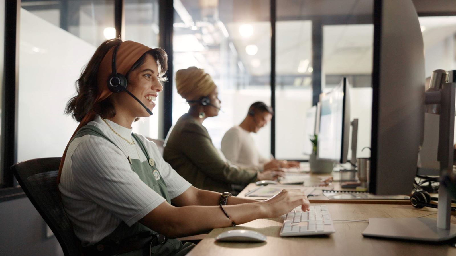 Women sat in an office with headsets on taking calls and smiling