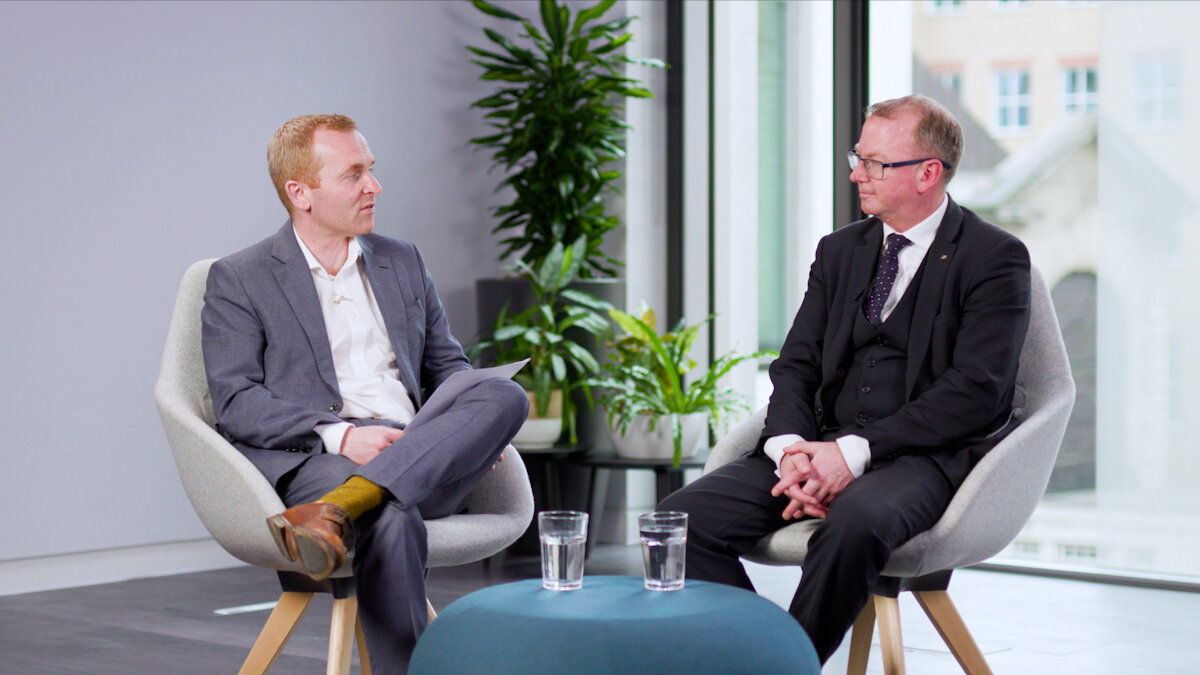 Callum Taylor from AXA financial lines and industry expert Martin Friel sat in grey chairs in front of a coffee table with plants behind them discussing Financial Lines