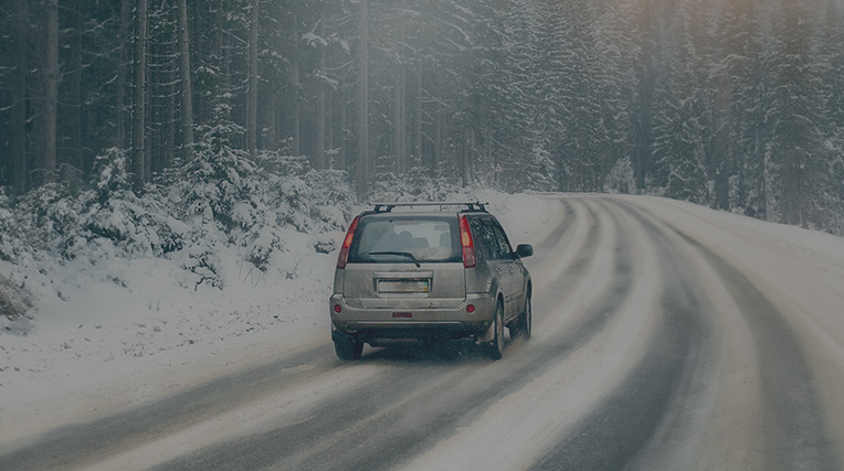 A 4x4 car on the road in snow surrounded by woods