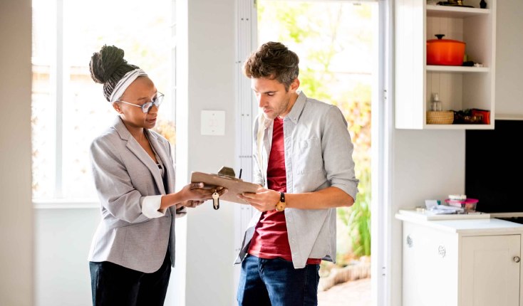 Letting agent handing tenant keys and a contract on a clipboard to sign for a rented home